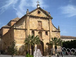 Convent facade with fountain and palm trees in the square.