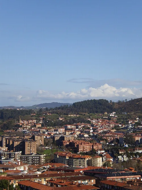 Paisaje urbano de Berango visto desde Algorta con colinas y cielo azul.