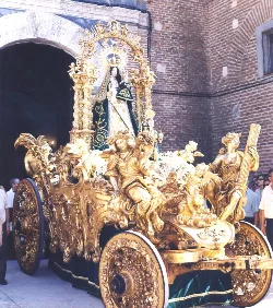 Image of a Virgin on a golden float with religious figures on the street.