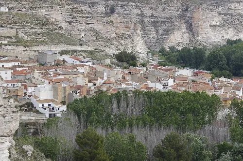 Vista de un pueblo con casas blancas y árboles en primer plano, con un acantilado de roca en el fondo.