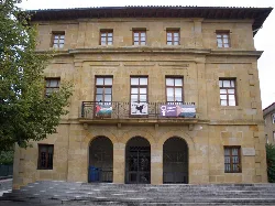 Edificio de piedra con tres arcos en la entrada y ventanas en la fachada.