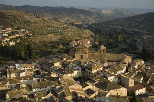Aerial view of old houses and a church in Pastrana, Guadalajara, with mountains in the background.