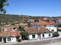Casas con tejados de teja y una calle en Fuentes de Béjar, con colinas al fondo.