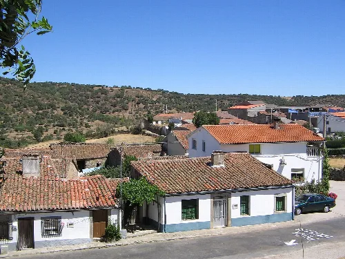 Casas con tejados de teja y una calle en Fuentes de Béjar, con colinas al fondo.