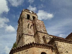Stone bell tower of a church with partly cloudy sky.
