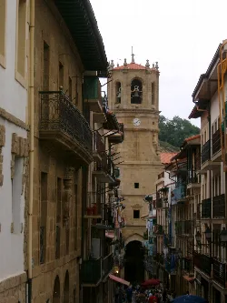 Torre de la iglesia de San Salvador en Getaria, Guipúzcoa, con edificios y balcones en primer plano.