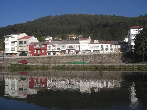 Houses by the Xuvia River in Neda, with green hills in the background.