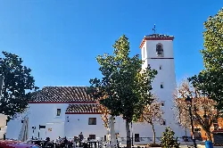 Weiße Kirche mit Turm und Bäumen auf dem Platz in Ogíjares.