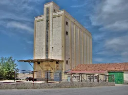 Large grain silo with concrete structure and cloudy sky.