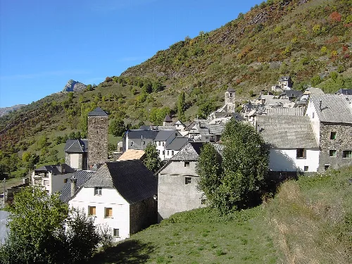 Dorf Gistaín an einem Hang mit Häusern und Türmen, umgeben von Vegetation und Bergen.