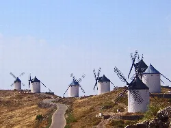 Sieben Windmühlen auf einem Hügel mit blauem Himmel und einem gewundenen Weg im Vordergrund.