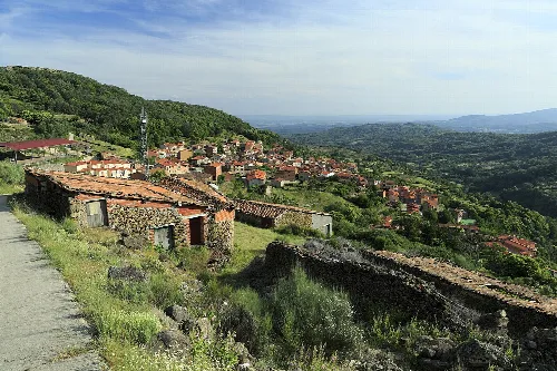 Hügeliges Dorf mit Häusern und Vegetation, im Hintergrund ein Tal.