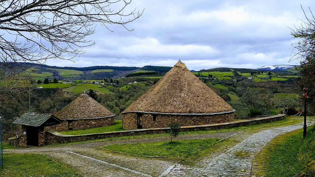 Group of stone pallozas with thatched roofs in a rural landscape.