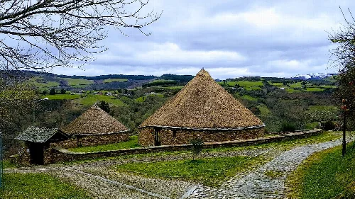Gruppe von Steinpallozas mit strohgedeckten Dächern in einer ländlichen Landschaft.