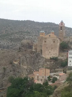 Iglesia de piedra con campanario y cúpulas en una colina rocosa.