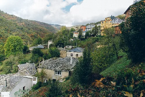 Häuser in einem Dorf auf den Hügeln von Caurel, Lugo, mit Vegetation und Bergen.