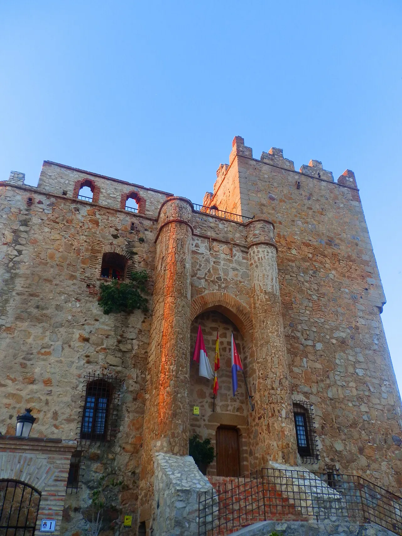 Stone castle with towers and flags at the entrance under a blue sky.