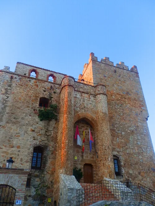 Castillo de piedra con torres y banderas en la entrada, bajo un cielo azul.