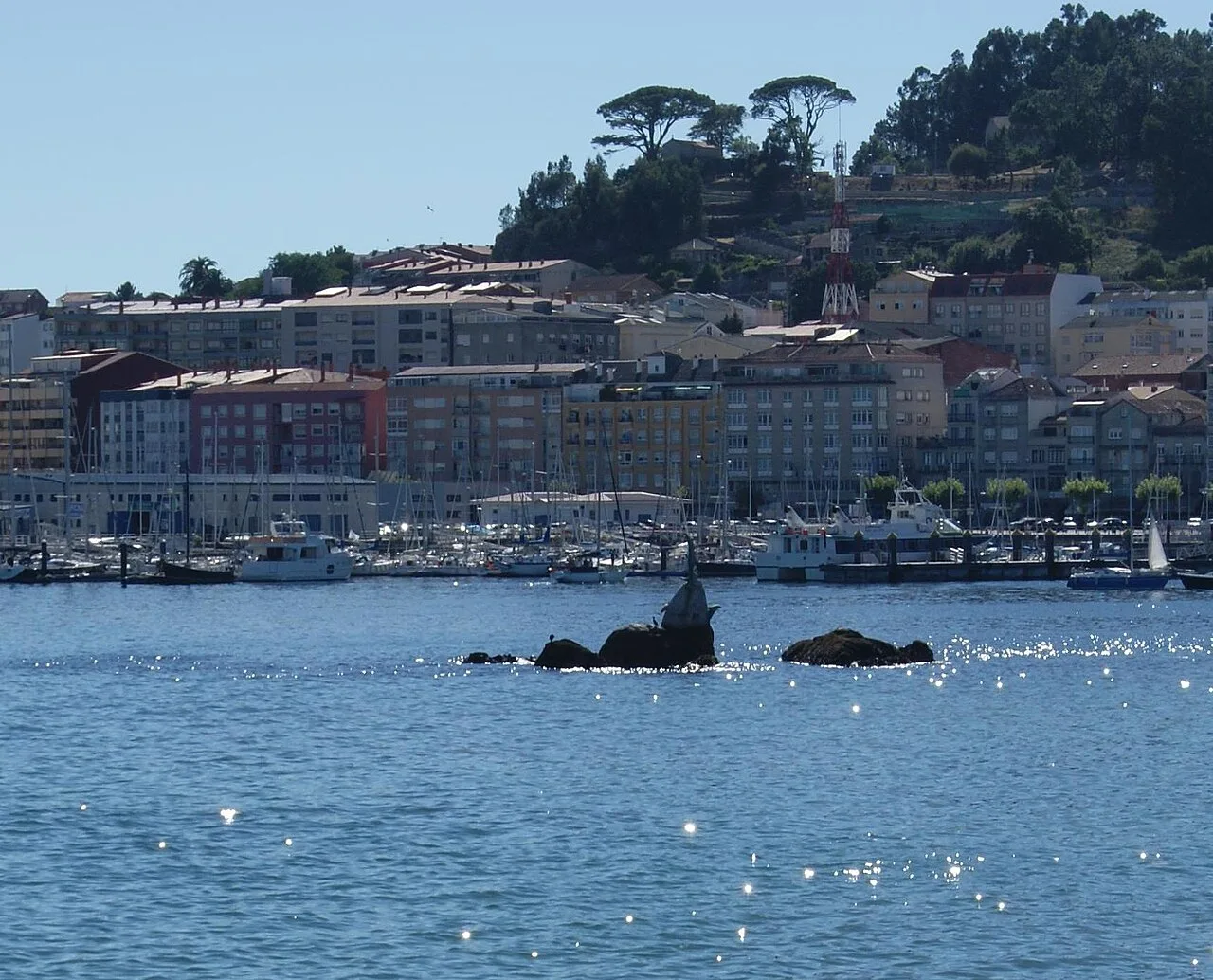 View of the port and buildings in Cangas de Morrazo, Galicia, with green hills in the background.