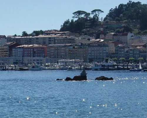 View of the port and buildings in Cangas de Morrazo, Galicia, with green hills in the background.