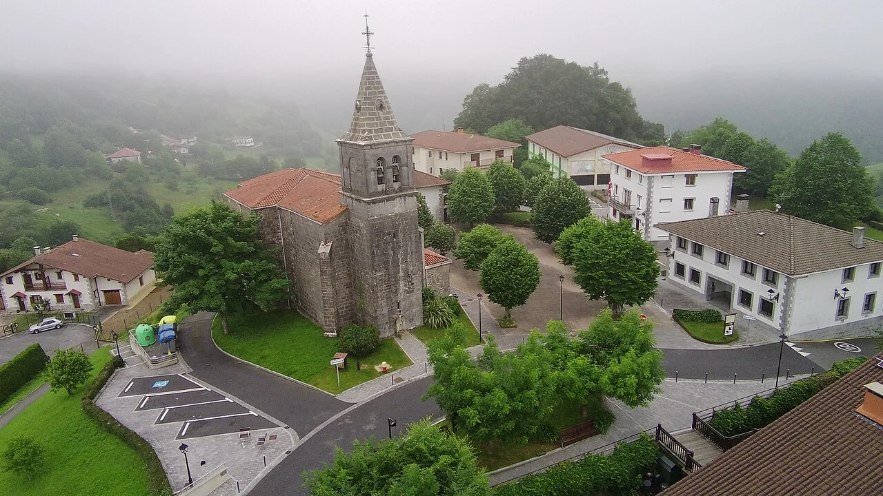 Vista aérea de la iglesia y casas en Leaburu con vegetación y niebla.
