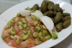Habas con tomate, bacalao, rábanos y aceitunas en un plato.