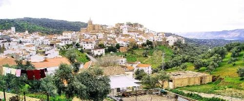 Vista de casas blancas en una colina con árboles y montañas al fondo.