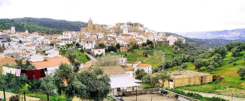 Vista de casas blancas en una colina con árboles y montañas al fondo.