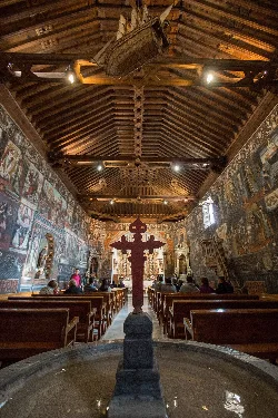 Interior of a church with fresco-decorated walls and wooden ceiling.