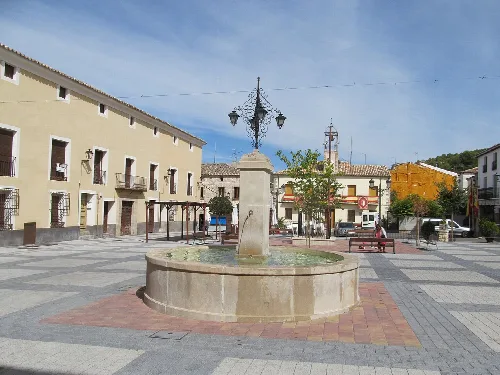 Fountain in the square with a lamp post and trees.