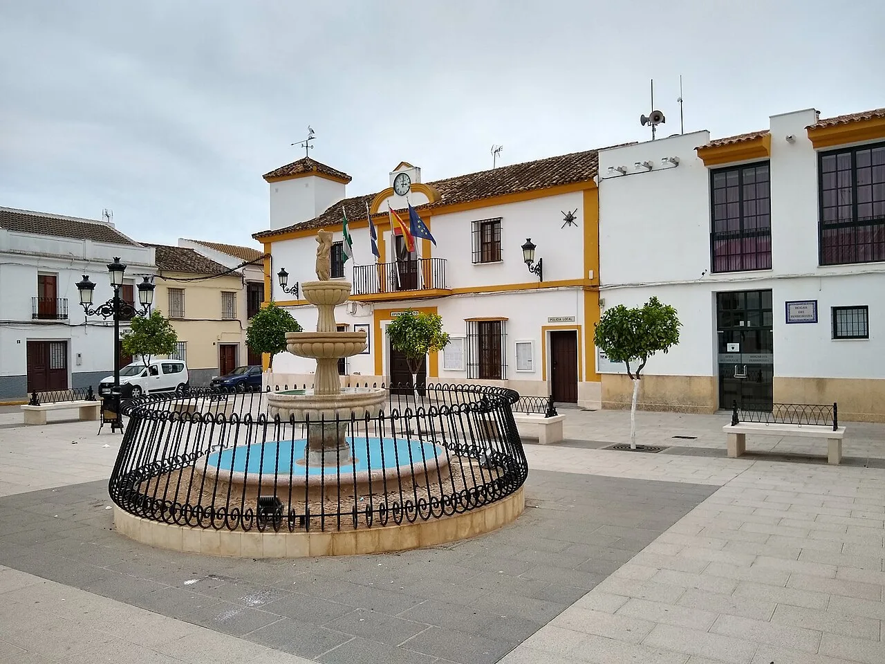 Fuente en la plaza con edificios blancos y árboles en Aguadulce.