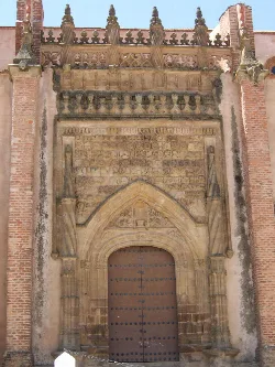 Fachada de una iglesia con puerta de madera y detalles góticos en Azuaga.