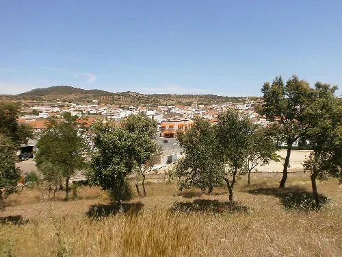 Blick auf Häuser und Bäume in Villar del Rey mit Hügeln im Hintergrund.