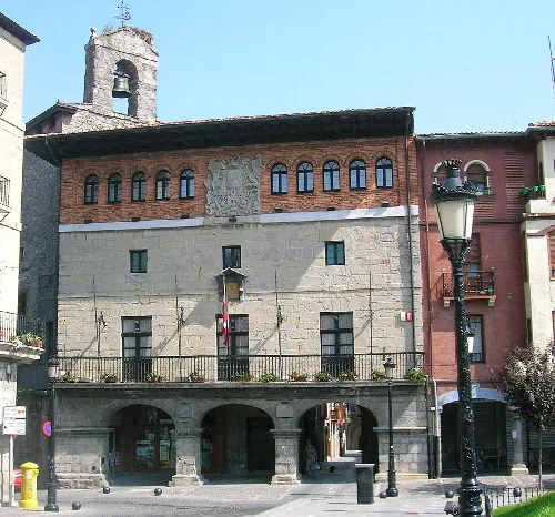 Edificio del ayuntamiento con fachada de piedra y ladrillo, y escudo en el centro.