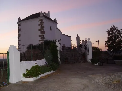 Weiße Kirche von Torreorgaz mit Calvario und Bäumen im Hintergrund.