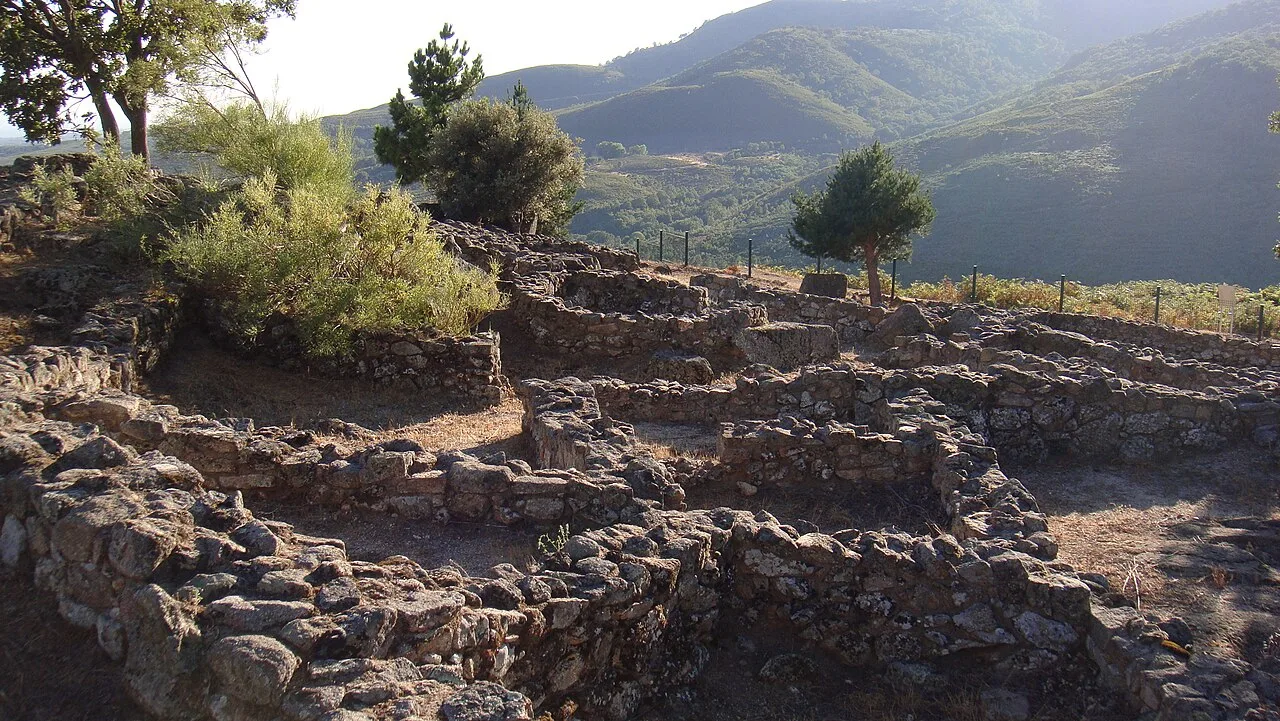 Steinruinen von Häusern an einer archäologischen Stätte mit Bergen im Hintergrund.
