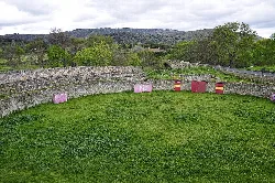 Old bullring with stone walls and green grass.