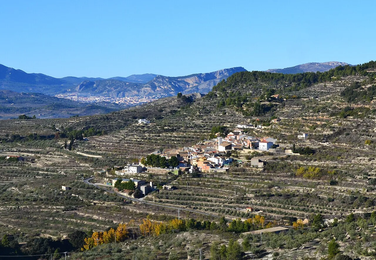 Paisaje de terrazas en las laderas con un pueblo en el centro y montañas al fondo.