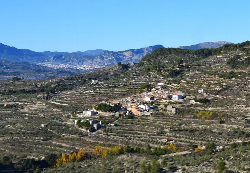 Terrassierte Landschaft mit einem Dorf in der Mitte und Bergen im Hintergrund.