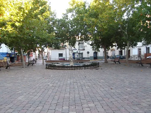 Main square of Porzuna with trees, benches, and stone pavement.