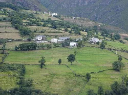 Grüne Wiesen mit verstreuten Häusern und Bergen im Hintergrund in Ibias, Asturien.