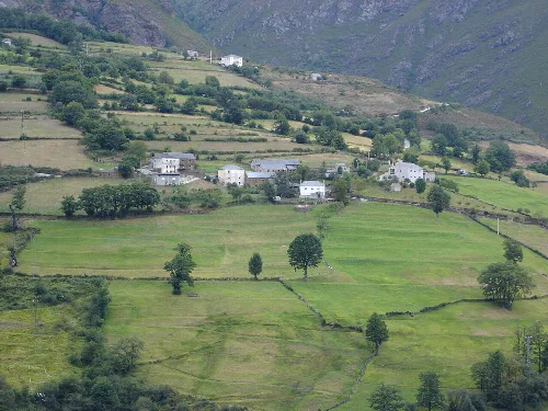 Paisaje de praderas verdes con casas dispersas y montañas en el fondo en Ibias, Asturias.