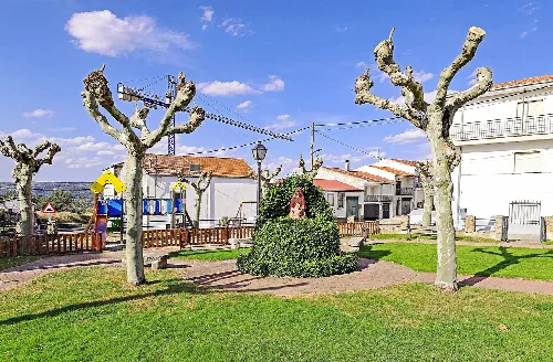 Parque con árboles podados, escultura y zona de juegos en Ledrada.