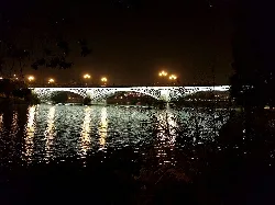 Iron bridge over the Guadalquivir River in Seville at night with lights.