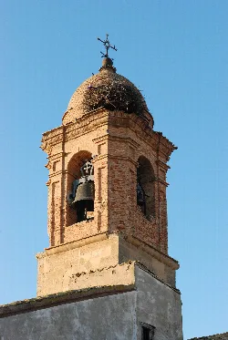 Brick bell tower with two bells and a cross at the top.