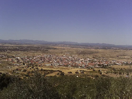 Luftaufnahme eines Ortes, umgeben von Feldern und Bergen im Hintergrund.