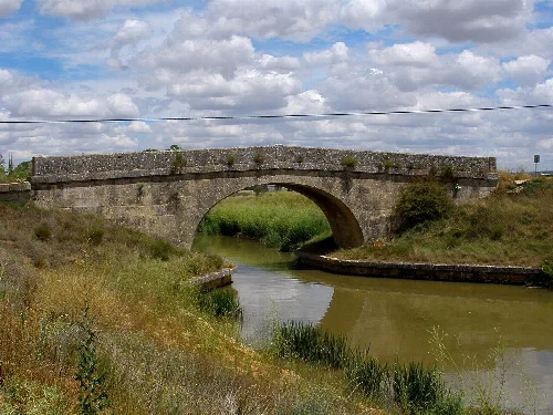 Stone bridge over the canal with cloudy sky and vegetation.