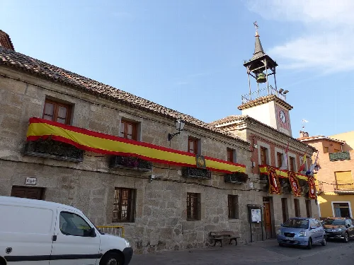 Main square of Mejorada with Spanish flags and parked cars.