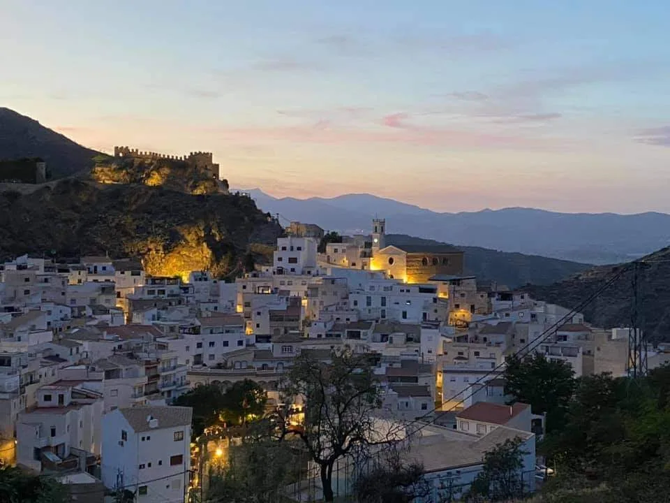 Paisaje de Sierro con casas blancas y castillo en la colina al atardecer.