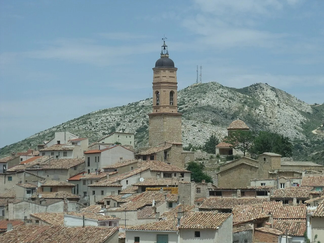 Vista de un pueblo con una torre de iglesia y casas en un entorno montañoso.